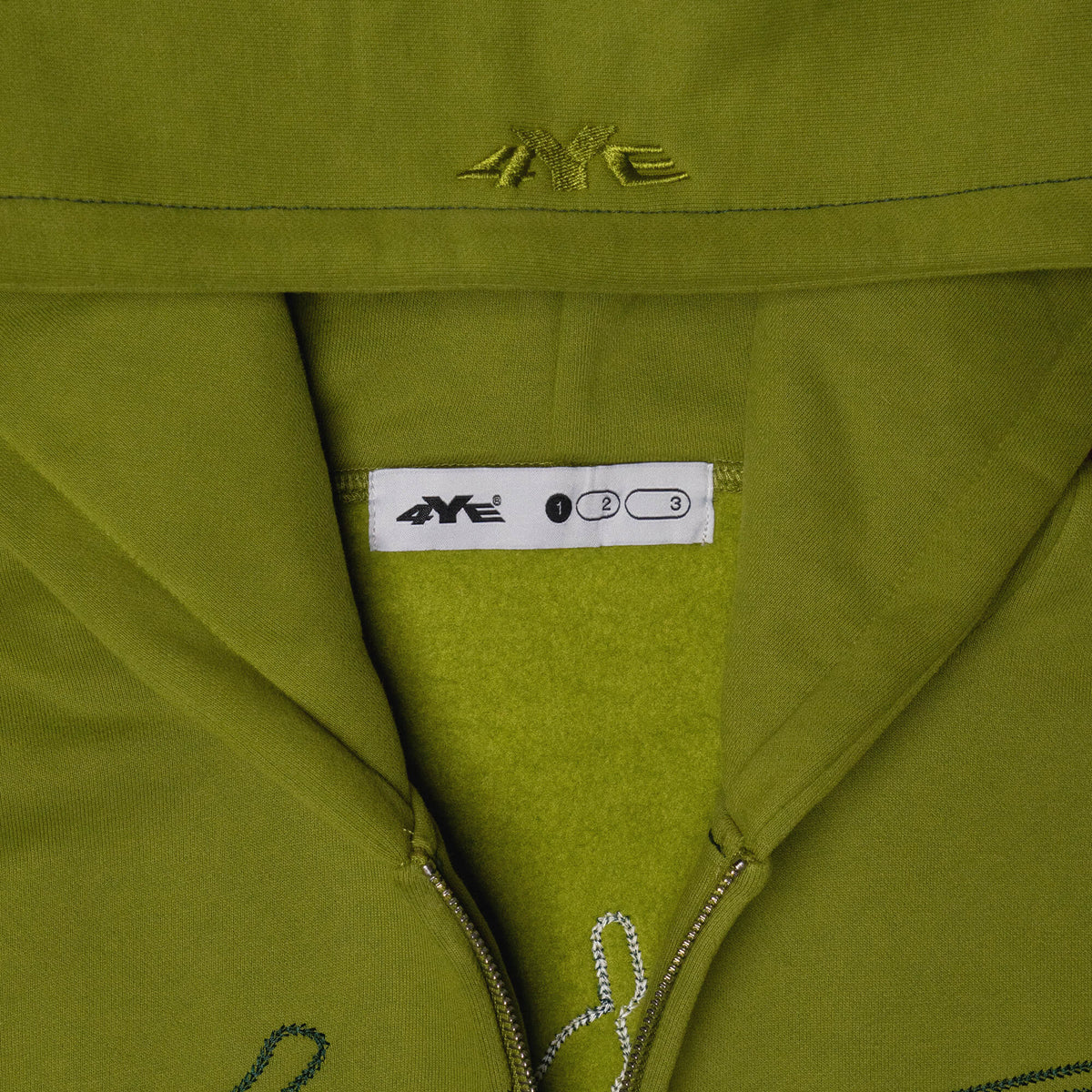 Close-up view of the 4YE Signature Logo Zip Hoodie in Matcha Green. The hoodie features 325 GSM brushed medium weight fleece offering ultimate comfort and warmth, including high-quality chain stitch embroidery and a 2-way YKK zipper, showcasing a trendy cropped and boxy fit.