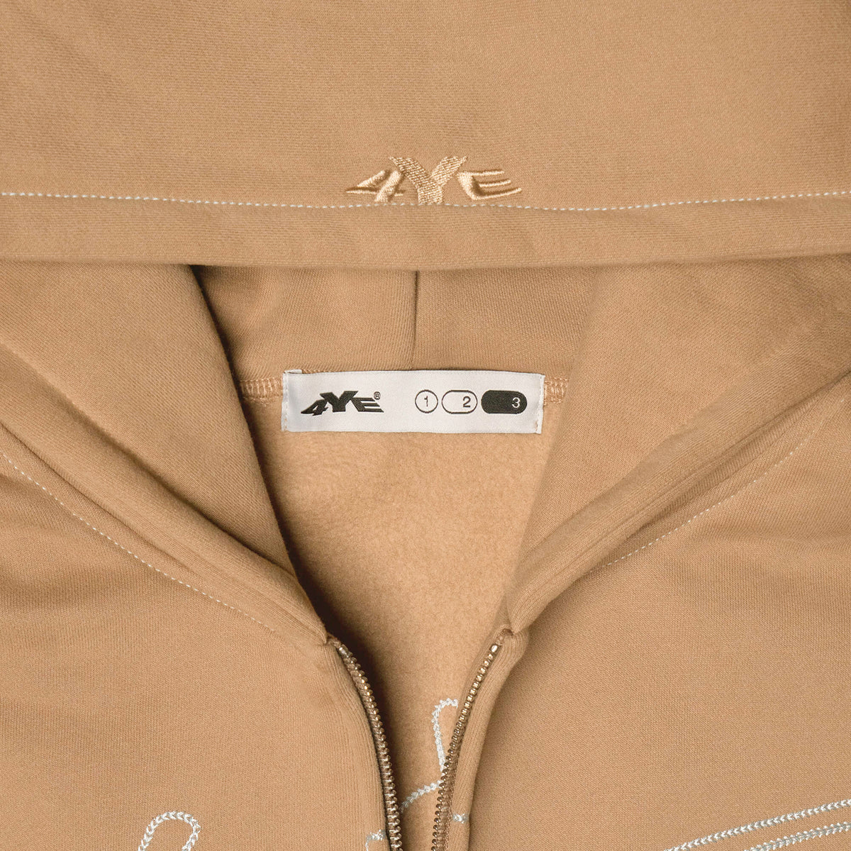 Close-up view of the 4YE Signature Logo Zip Hoodie in Light Brown. The hoodie features 325 GSM brushed medium weight fleece offering ultimate comfort and warmth, including high-quality chain stitch embroidery and a 2-way YKK zipper, showcasing a trendy cropped and boxy fit.